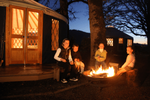 Four kids sitting around a campfire in front of a Pacific Yurt.