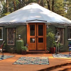 Yurt on a wooden patio with outdoor furniture and rugs.