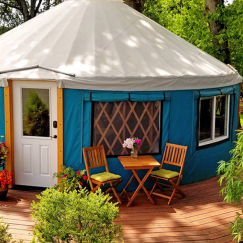 Small Pacific Yurt with a blue tarp and tan roof in a backyard garden.
