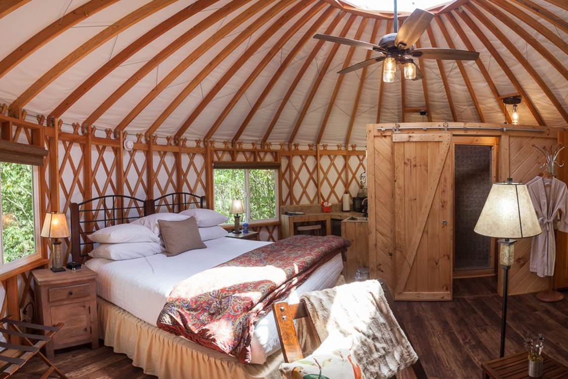 Queen size bed in a yurt bedroom with a large two door dresser and hanging fan.