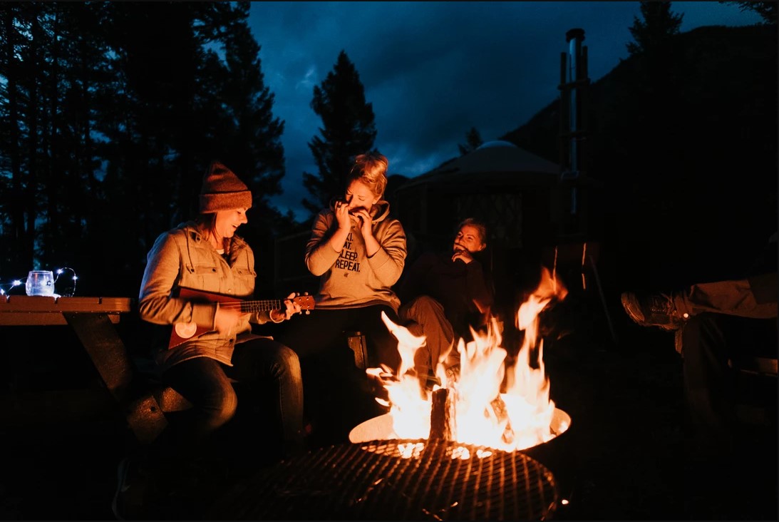 Three people sitting around a campfire playing instruments at Radius Retreat.