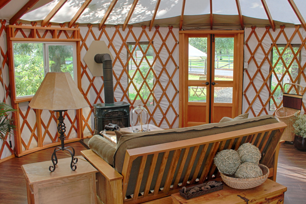 Wooden couch with tan cushions in front of a coffee table and wood fire stove inside a yurt.