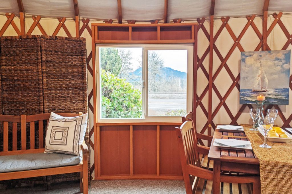 Wooden bench to the left of a yurt window and a kitchen table to the right of the window.
