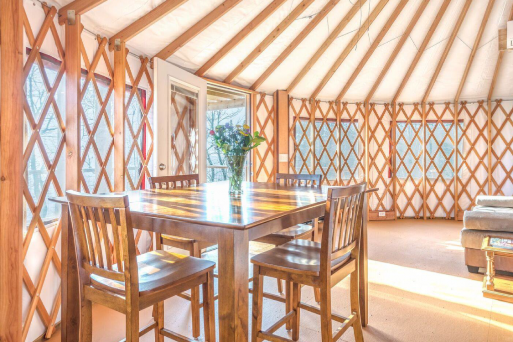 Four-seat wooden table with a flower arrangement on top, inside the living space of a Pacific Yurt.