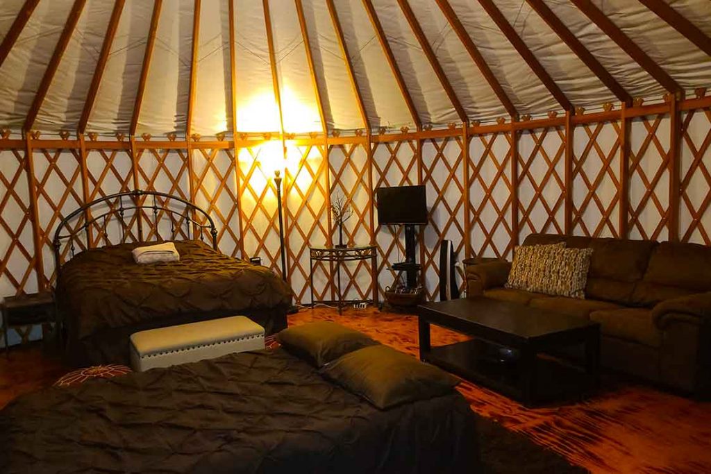 A queen bed and a full-size sleeper, complete with cozy bedding, blankets, and pillows inside a Pacific Yurt.