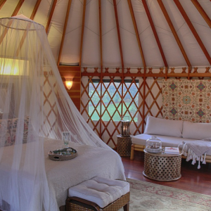 Queen sized bed with a decorative bed hanging inside a Pacific Yurt.