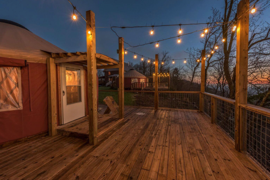 Wooden deck surrounding a Pacific Yurt illuminated by hanging lights.