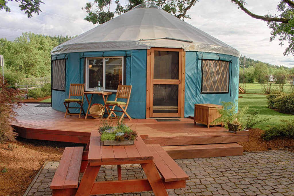 Pacific Yurt with a light blue canvas, a wooden deck surrounding the structure, and a picnic table outside.