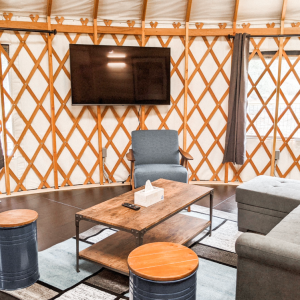 Living room with a couch, wooden coffee table, and a TV mounted on a yurt lattice wall.