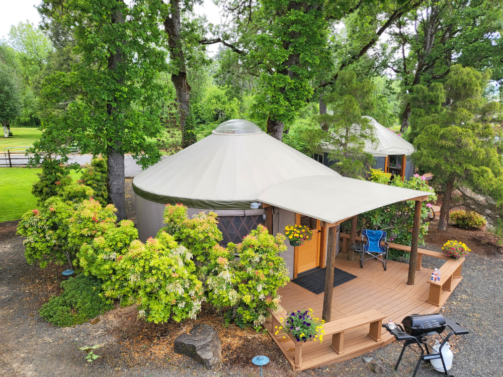 A Pacific Yurt with a front door canopy and a wooden front porch surrounded by small trees.