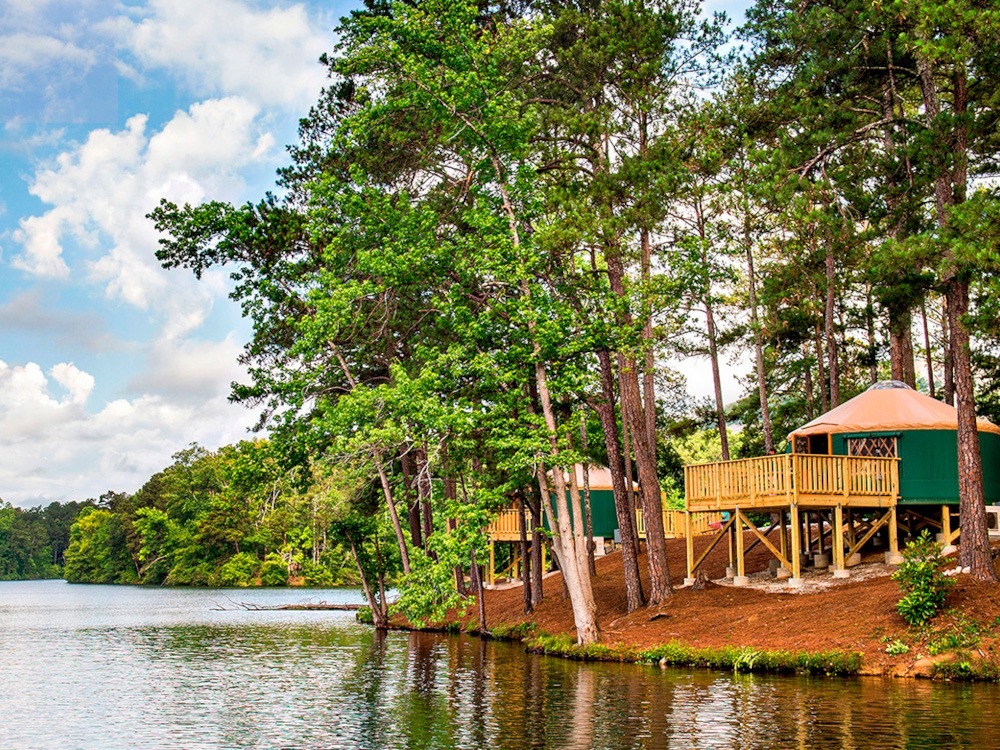 A Pacific Yurt with a green and white canvas and a wooden deck overlooking the edge of a lake.