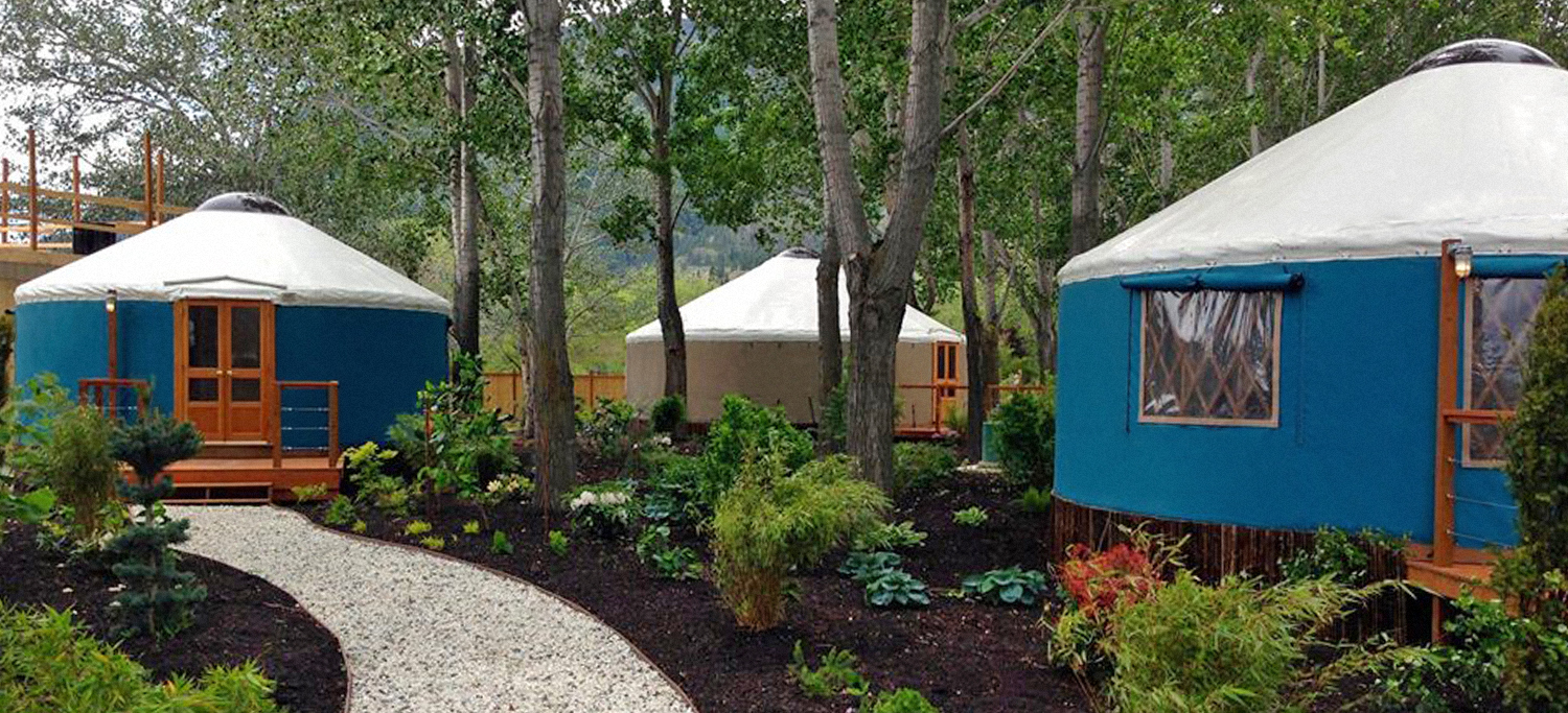 Three Pacific Yurts with wooden front porches on a tailored campsite with stone pathways and flower beds.