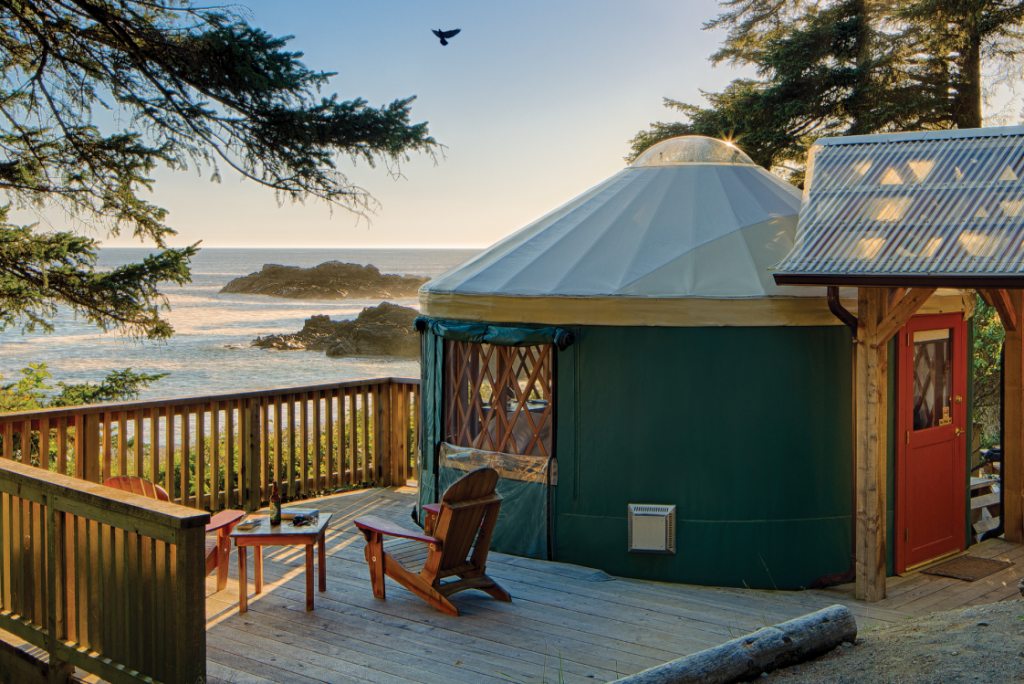 Pacific Yurt on the coast with a wooden deck with two Adirondack chairs and a small side table.